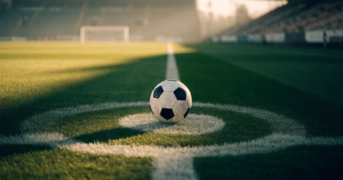 Uma bola de futebol no ponto central de um relvado, à luz da manhã