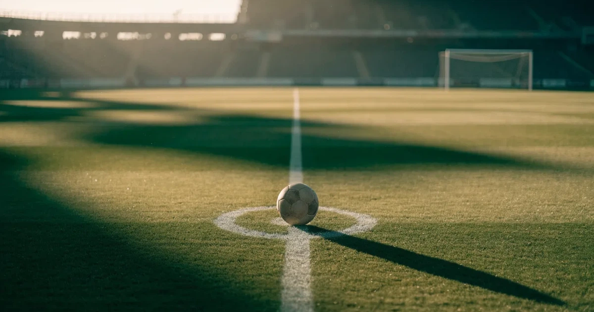 Uma bola de futebol no ponto central de um relvado, à luz da manhã
