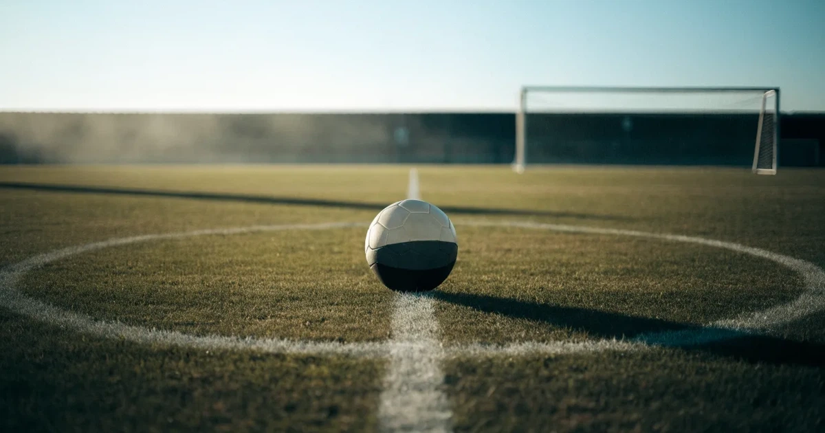 Uma bola de futebol no ponto central de um relvado, à luz da manhã